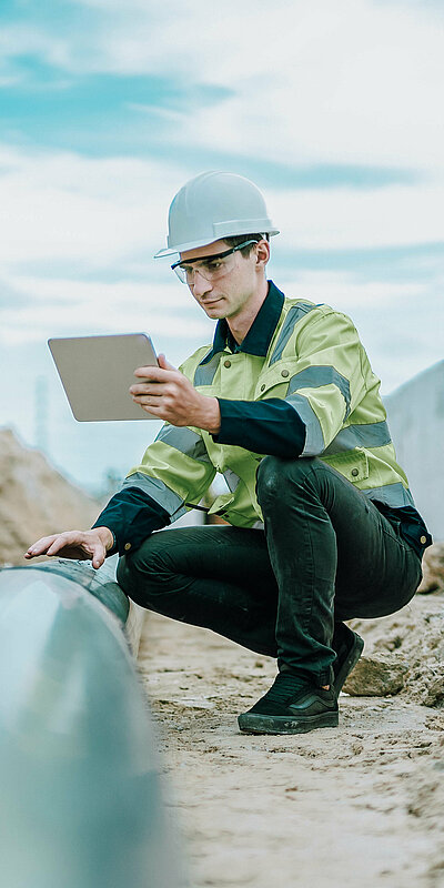 Arbeiter auf Baustelle in Hocke mit Tablet in der Hand