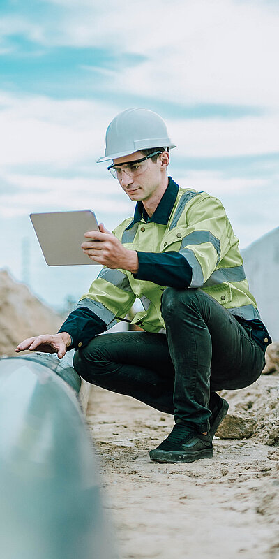 Arbeiter auf Baustelle in Hocke mit Tablet in der Hand