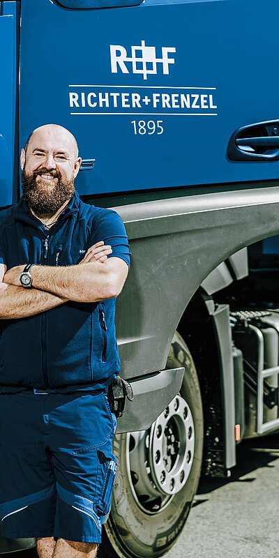 LKW-Fahrer mit verschränkten Armen vor einem Tiefbau-LKW